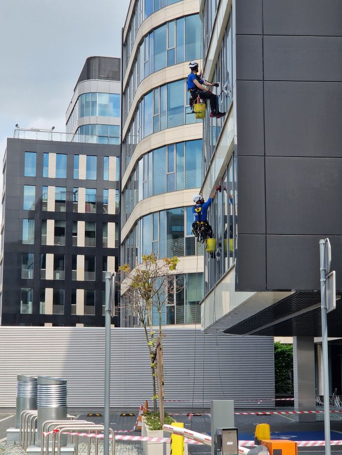 project-02-d Two workers clean windows on a tall office building in a city setting.